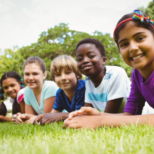 Five kids in a row on the grass, lying on their stomachs and smiling.