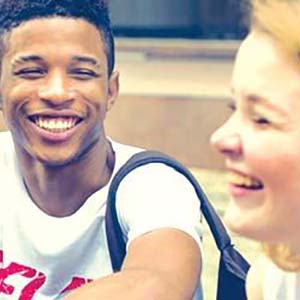 Two smiling teen students sitting outside on the steps of a building.