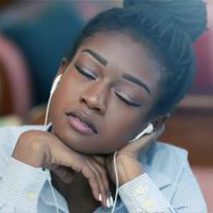 A person wearing earbuds, listening to music with their eyes closed.