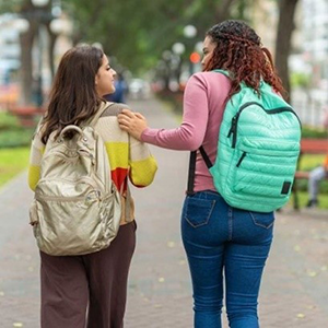 Two students wearing backpacks, walking outside and speaking with each other.